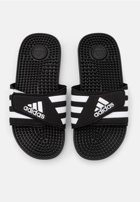 Mustat liukusandaalit, joissa on kolme valkoista raitaa, teksturoitu kumipohja, jossa on kohoumia, ja säädettävä remmi.