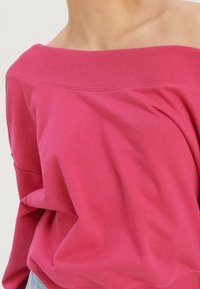 Felpa rosa a spalle scoperte realizzata in morbido misto cotone. Presenta un collo a coste e una vestibilità rilassata con delicati drappeggi.