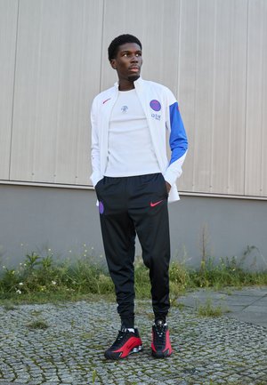 White jacket with blue accents, black Nike pants, and red-accented sneakers. Features round logos and a casual fit. Textured fabric.