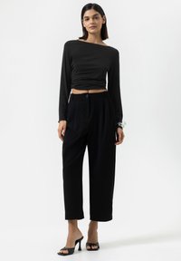 Haut noir à manches longues avec un décolleté asymétrique, associé à un pantalon large noir taille haute et des talons ouverts noirs.