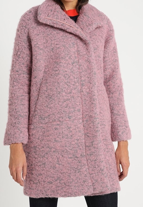 Manteau en laine rose texturée à manches longues avec grand col porté sur un pantalon noir et un haut rouge.