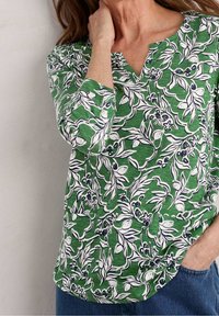 Grünes Oberteil mit floralen Mustern in Weiß und Marineblau, V-Ausschnitt und drei Viertelärmeln; weicher Stoff und entspannter Schnitt.