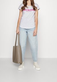 Šedé tričko s růžovým nápisem "True Religion", světle modré volné džíny, krémové kotníkové boty a hnědá texturovaná taška.