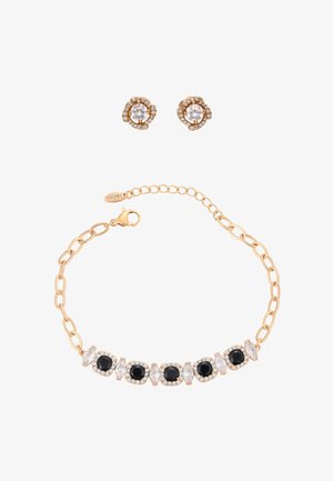 Gouden armband met afwisselend zwarte en heldere edelstenen, en bijpassende gouden oorstekers met heldere edelstenen omringd door kleinere stenen.