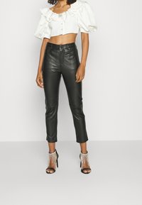 Svarta läderbyxor i kort modell med smal passform, med framfickor; kombinerat med en kort vit blus med puffärmar och dekorativa knappar.