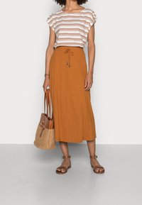 Top de manga corta a rayas en blanco y óxido, combinado con una falda de canalé color óxido con cordón. Sandalias planas marrones y un bolso de mimbre completan el look.