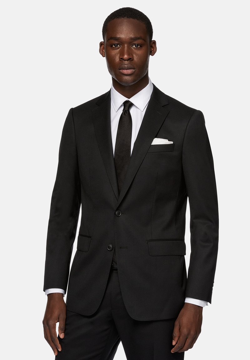 Černý upravený oblek s klopovými límci, dvěma knoflíky a kapsami. Bílé košile a černá kravata, s kapesníčkem v náprsní kapse.