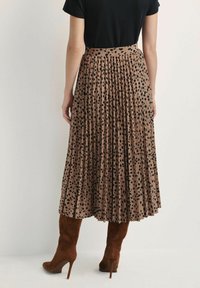 Plisowana spódnica midi w beżowym materiale z czarnymi kropkami. Posiada wysoki pas i swobodny krój, zestawiona z brązowymi botkami do kolan.