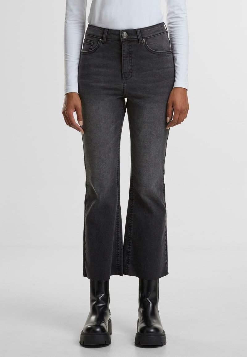 Jean noir taille haute avec une coupe évasée, dotée de poches avant et d'un zip, associée à des bottes noires chunky. Denim texturé.