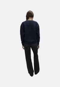 Felpa blu navale con scollatura a girocollo, vestibilità ampia, polsini e vita a coste, abbinata a jeans scuri a palazzo, vista da dietro.
