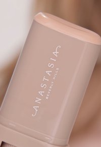 Beżowy cylindryczny korektor z gładką pokrywką. "ANASTASIA BEVERLY HILLS" jest wytłoczone na białym tle na korpusie.