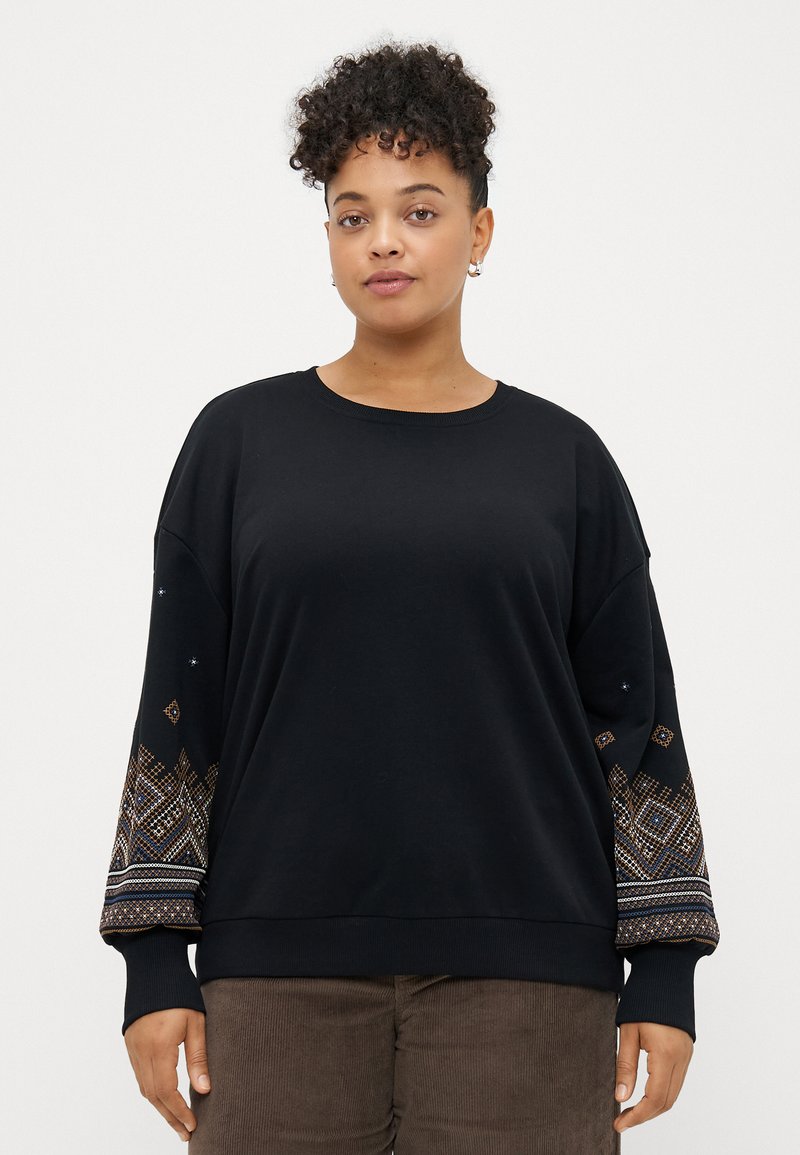 Μαύρη μπλούζα με μακριά μανίκια που διαθέτει περίπλοκα κεντήματα σε αποχρώσεις μπλε, πορτοκαλί και λευκού γύρω από τους μανικιού.