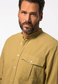 Camicia button-up in lino khaki con colletto alla mandarino, taschino applicato singolo e bottoni bianchi, che mette in risalto una finitura in tessuto testurizzato.
