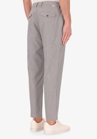 Pantaloni a strisce grigie e bianche con gamba affusolata, realizzati in un tessuto leggero, dotati di tasche posteriori e chiusura a bottone.
