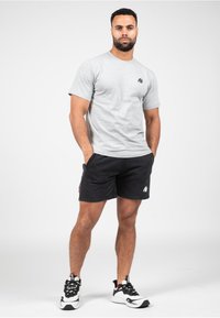 Grijze katoenen t-shirt met een zwart logo op de borst, gecombineerd met zwarte shorts met een wit logo en accenten, afgewerkt met zwart-witte sneakers.