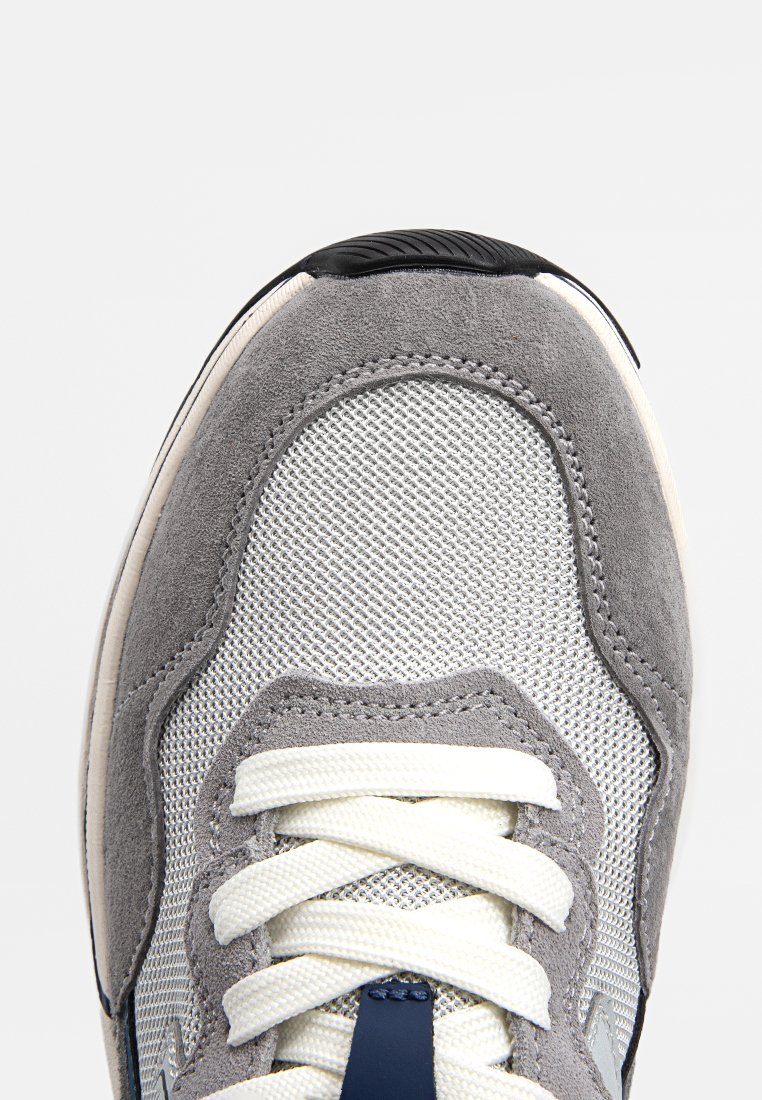 Grauer Sneaker mit einem Mesh-Obermaterial, Wildlederakzenten, weißen Schnürsenkeln und einem navyblauen Detail. Verfügt über eine abgerundete Zehenpartie und eine strukturierte Gummisohle.