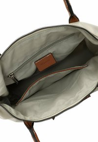 Interno grigio chiaro di una borsa a tracolla con chiusura a zip, dotata di una tasca con zip e un compartimento aperto, con dettagli in pelle marrone.