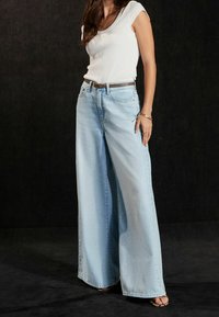 Un jean large bleu clair, en denim, avec une taille haute et une coupe structurée. Associé à un t-shirt blanc ajusté.