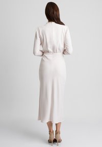 Sukienka midi z długim rękawem w jasnoróżowym satynie, z wcięciem w talii, zamkiem błyskawicznym z tyłu i gładką fakturą. Szpilki w kolorze beżowym z paskami na kostkach.