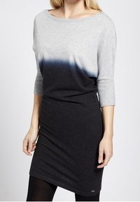 Graues Ombre-Kleid mit Dreiviertelärmeln, das von hellgrau zu dunkelgrau übergeht, und mit einer weichen Stricktextur sowie einer lockeren Passform ausgestattet ist.