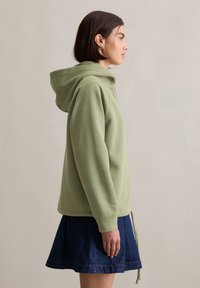 Groene hoodie van zacht materiaal, met een trekkoordkap, lange mouwen en een losse pasvorm, gecombineerd met een spijkerrok.