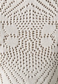 Kermanen kudottu kangas vaaleassa värissä, jossa on geometrisia kuvioita. Sisältää avonaisia neuleita ja teksturoituja alueita, jotka luovat yksityiskohtaisen visuaalisen vaikutelman.