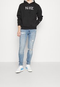 Svart Nike-hoodie med en framficka och snörning i huvan, kombinerad med ljusblå slitna tight jeans och vita sneakers med blå detaljer.