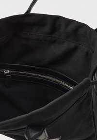 Czarna torba na zakupy z wewnętrzną kieszenią na zamek błyskawiczny. Posiada mocne uchwyty, miękką teksturę i minimalistyczny design.