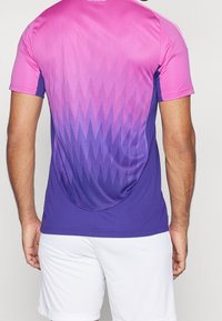 Camiseta atlética de manga corta con un degradado de rosa a púrpura y un patrón geométrico. Hecha de tela ligera, con una textura suave.