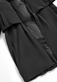 Cappotto lungo nero con fodera interna visibile, zipper frontale parzialmente aperta e due tasche laterali su uno sfondo bianco.
