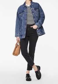 Persona con chaqueta de mezclilla azul, jeans negros de talle alto, mocasines negros, camiseta a rayas y sosteniendo un bolso marrón peludo.