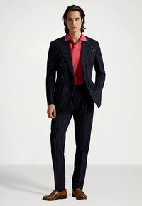 Κοστούμι ναυτικού μπλε με ρίγες, με διπλό πεδίο σακάκι, σε συνδυασμό με ροζ πόλο πουκάμισο. Καφέ παπούτσια ολοκληρώνουν την εμφάνιση, τονίζοντας το σύγχρονο ράψιμο.