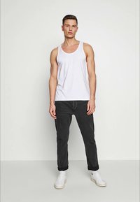 Débardeur en coton blanc, jean en denim noir et baskets blanches. Coupe droite avec des poignets retroussés, détails minimalistes et design décontracté.