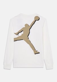 Vit långärmad skjorta med en stor grafik av en hoppande figur i guld och svart, med rund krage och mjuk textur.
