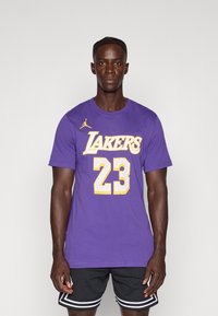 Ljubičasta majica s natpisom "Lakers" i brojem "23" u žutom printu, s malim žutim Jordan logotipom na lijevom ramenu.
