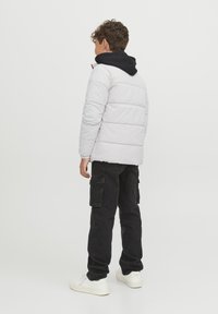 Vadderad vit jacka med svart huva, kombinerad med svarta cargobyxor och vita sneakers, sedd bakifrån. Slät struktur, formad passform.