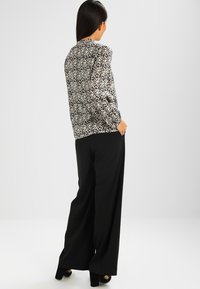 Blusa a maniche lunghe con motivo floreale in bianco e nero, abbinata a pantaloni larghi neri e scarpe con tacco.