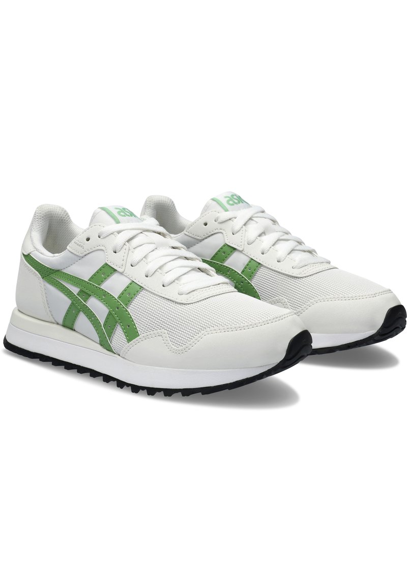 Zapatillas deportivas blancas con detalles en verde, con una parte superior de malla, suela de goma y un diseño clásico de cordones. Logo destacado en la lengüeta.