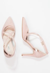 Rosa högklackade skor i mocka med metalliska detaljer, spetsiga tår och korsande remmar med ankelstängning.