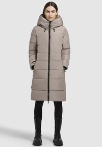 Long beige puffer coat with a hood, featuring a front zipper, horizontal quilted sections, and side pockets, paired with black combat boots.