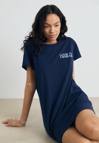 Marinblå T-shirt klänning i mjuk bomull med korta ärmar. Har "LOVE TO DREAM" broderat i vitt framtill. Slät textur.