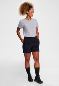 Gray cotton t-shirt with short sleeves, black shorts, and knee-high black socks. Notable logo detail on the shirt and shorts. Black athletic shoes.