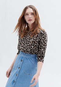 Långärmad topp i leopardmönster parat med en högmidjad jeanskjol med knäppning fram och bred midja.