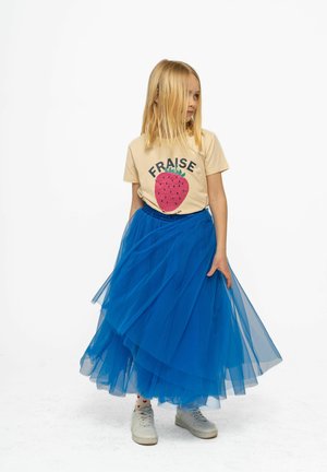 T-shirt beige chiaro con grafica di fragola rosa, abbinato a una gonna di tulle blu a strati e scarpe da ginnastica bianche.