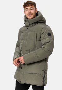 Padded jacket in olive green with a high collar, hood, front button closure, and multiple pockets. Textured fabric with structured quilting.