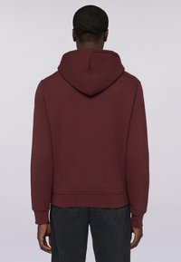 Burgundowa bluza z kapturem na sznurki, ściągacze przy rękawach i u dołu; miękka tkanina o gładkiej fakturze; noszona z ciemnymi dżinsami.
