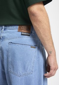 Lyseblå denim jeans med en læderpatch med præget detaljering. Et lille sort "VOLCOM" logo tag på den bageste lomme.