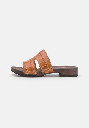 Sandalia tipo slide de cuero color caramelo con textura de cocodrilo, dos tiras anchas y un tacón bajo de madera. Diseño sencillo con superficies lisas y detalles mínimos.