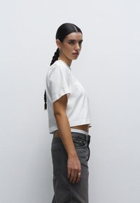 Camiseta blanca cortada de manga corta, combinada con jeans grises de cintura alta. Textura suave, diseño sencillo, ajuste sutil.