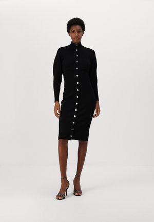 Gehaakte zwarte jurk met een hoge kraag, knoopsluiting aan de voorkant, lange mouwen en een getailleerd silhouet. Zilveren knopen langs het midden voegen detail toe.